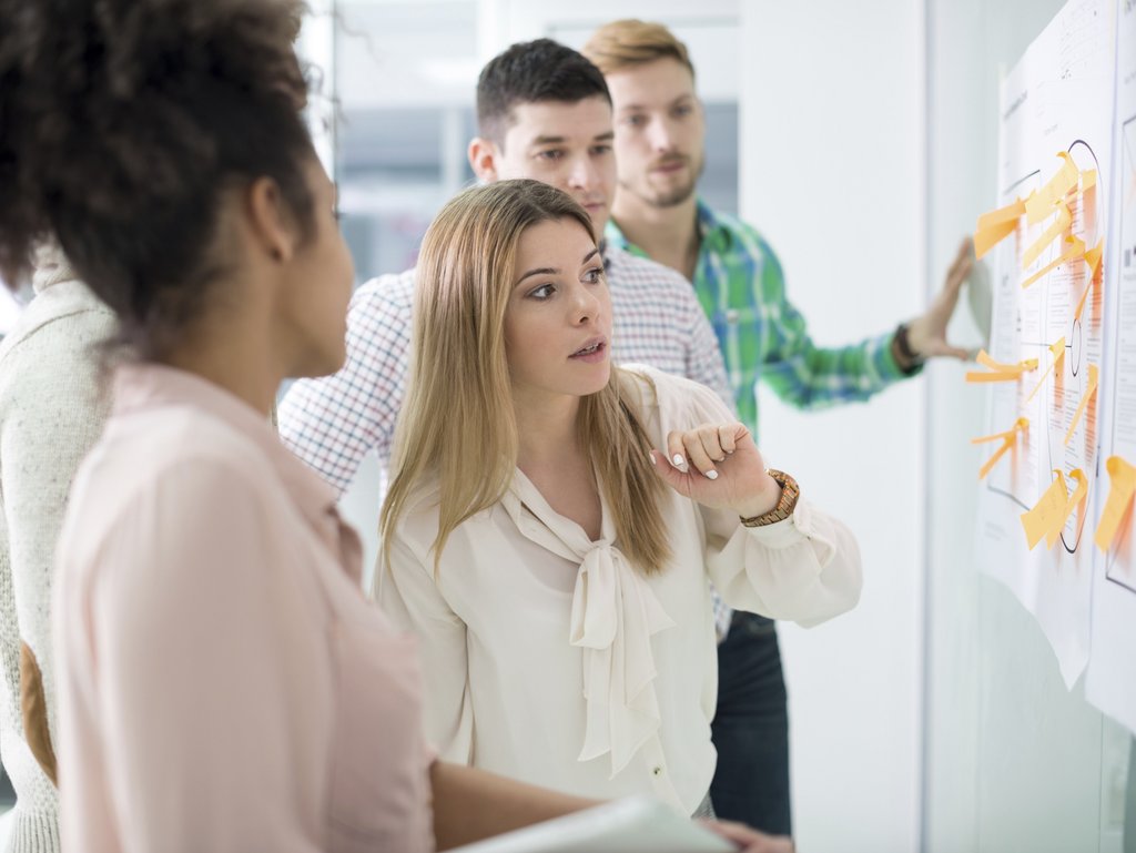 A diverse group of men and women in front of a whiteboard with post-it notes on it.