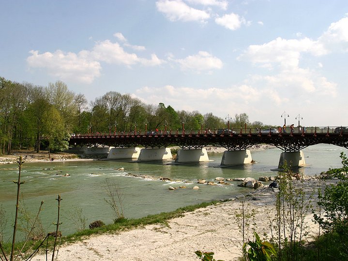 An iron and concrete bridge with the Isar flowing under it surrounded by trees