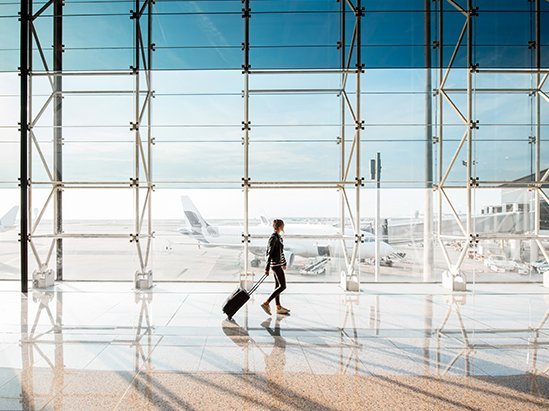 View on the aiport window with woman walking with suitcase at the departure hall of the airport. Wide angle view.