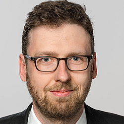 Headshot of Matthias Uhl, a young man smiling on a simple grey background.